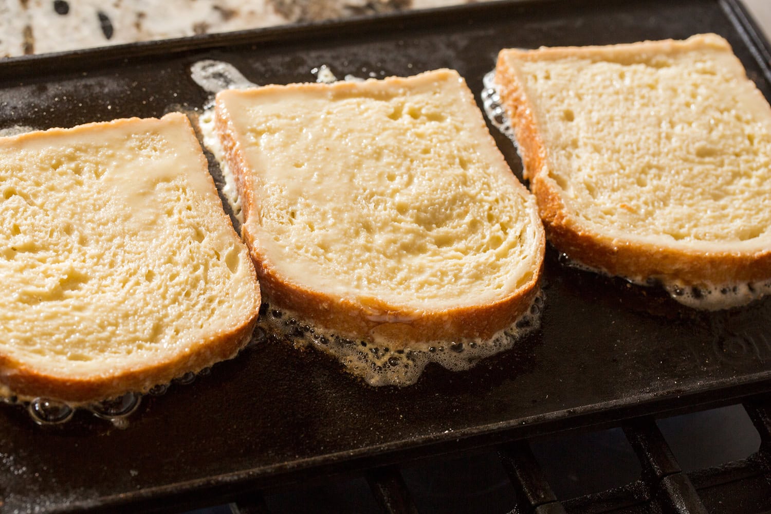 Raw french toast cooking on first side on griddle with butter.