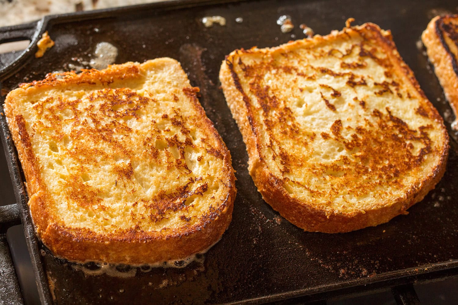 Slices of french toast cooking on cast iron griddle on second side.
