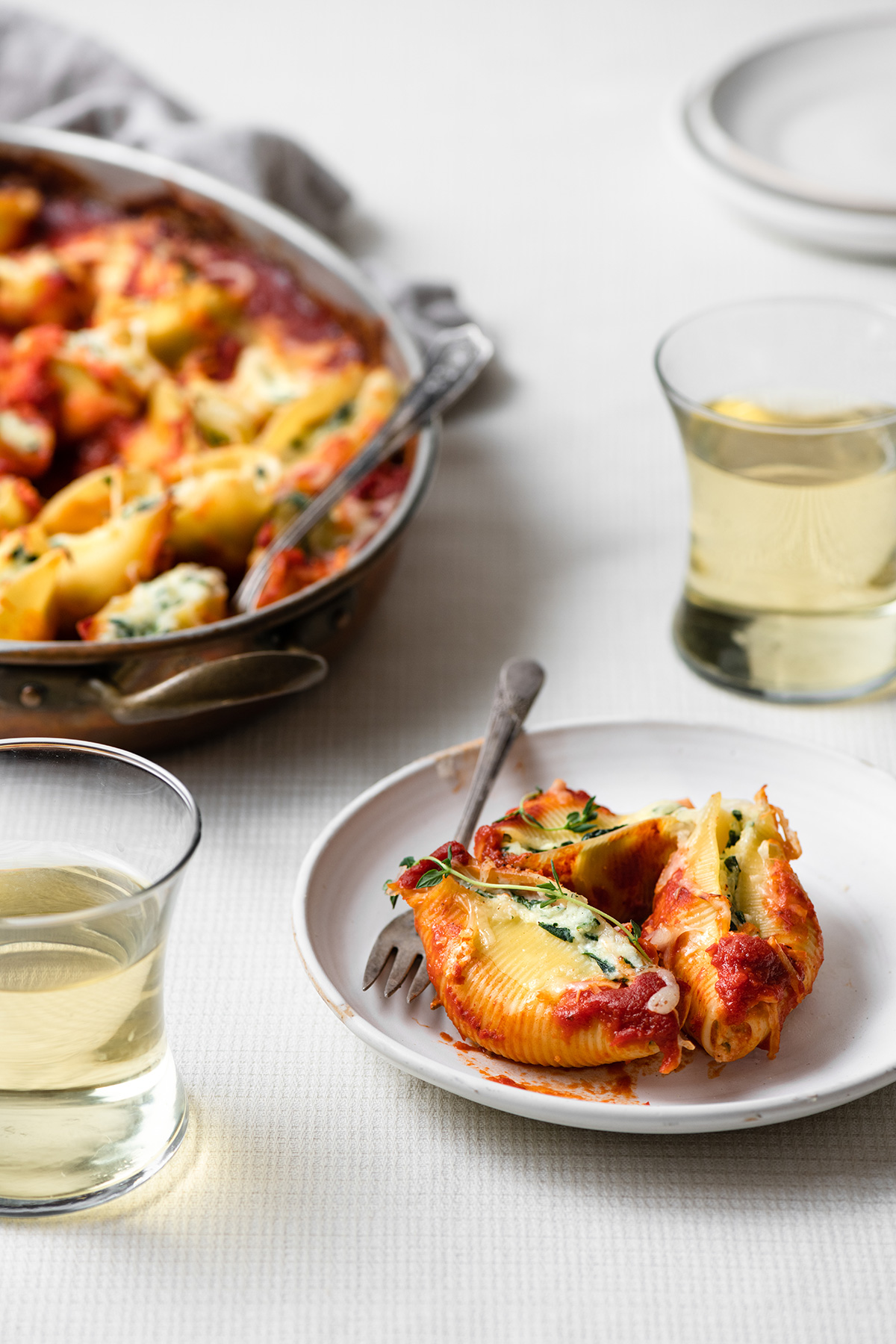 Stuffed shells on a white serving plate with the baking dish of stuffed shells in the background.