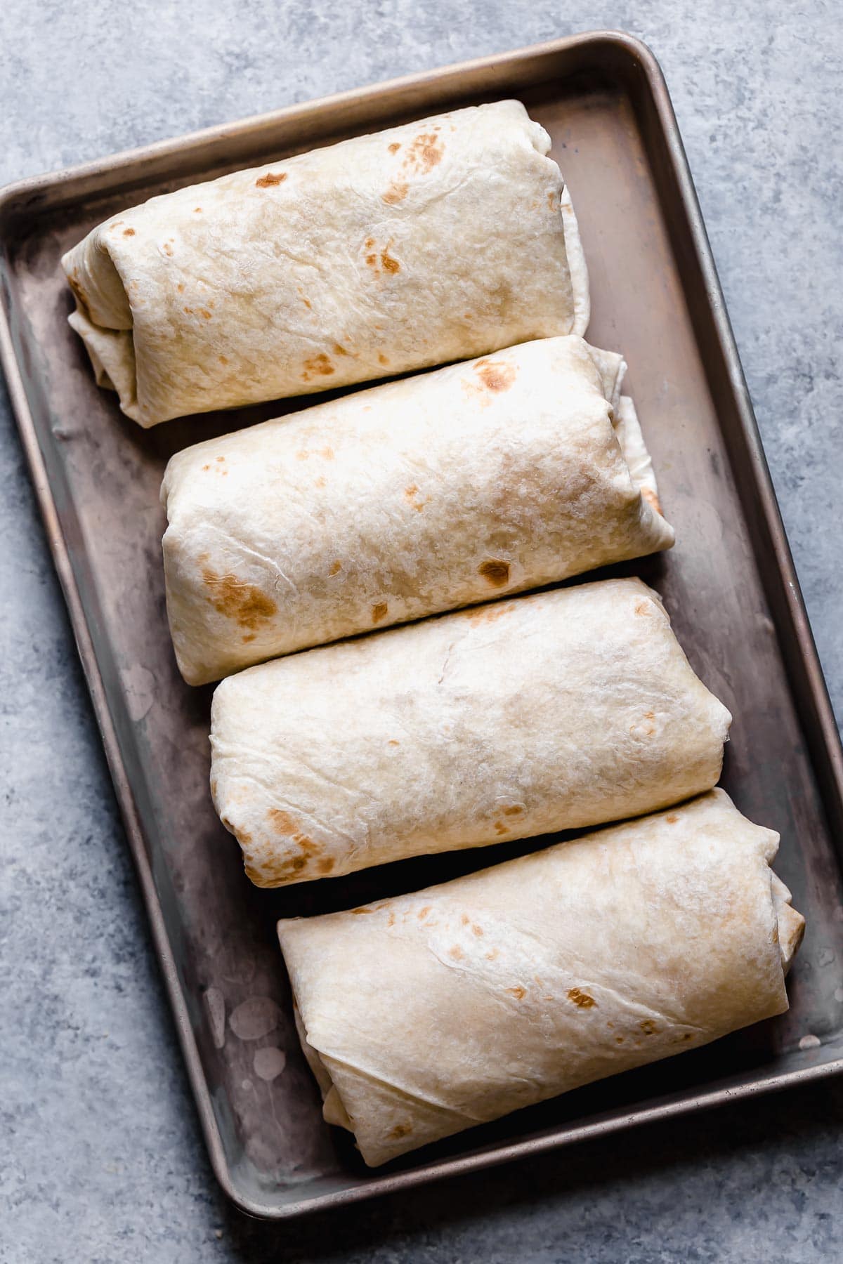 Four assembled homemade chimichangas in a row before frying.