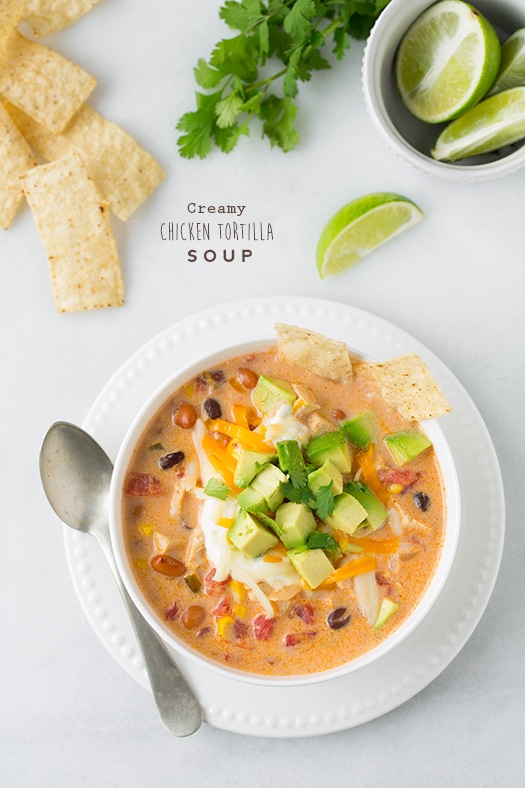 An overhead shot of Creamy Chicken Tortilla Soup in a bowl topped with avocado and lime wedges at the side