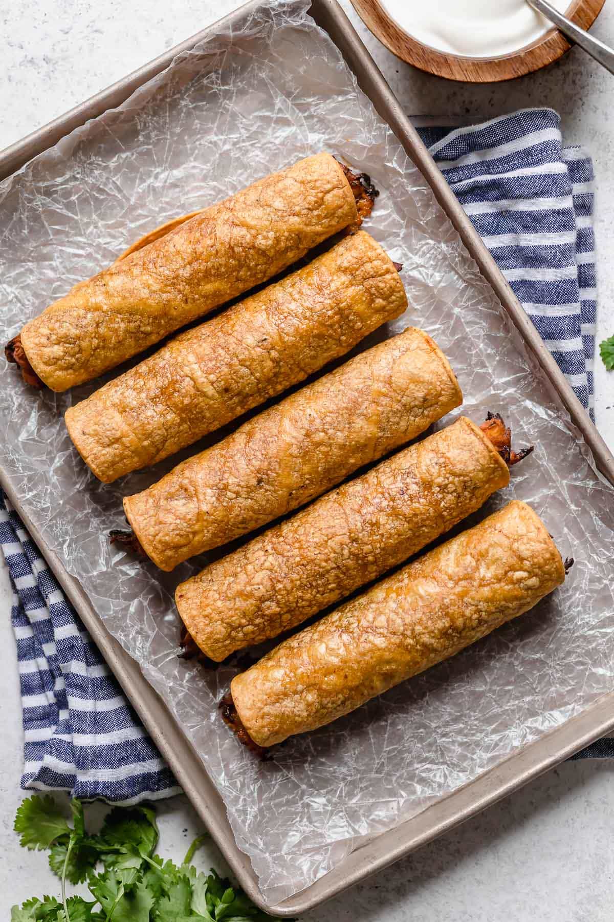 Rolled chicken taquitos on a baking sheet before baking.