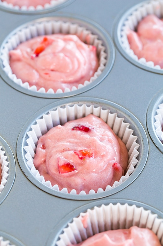A process shot of filling cupcake cases with strawberry cupcake batter