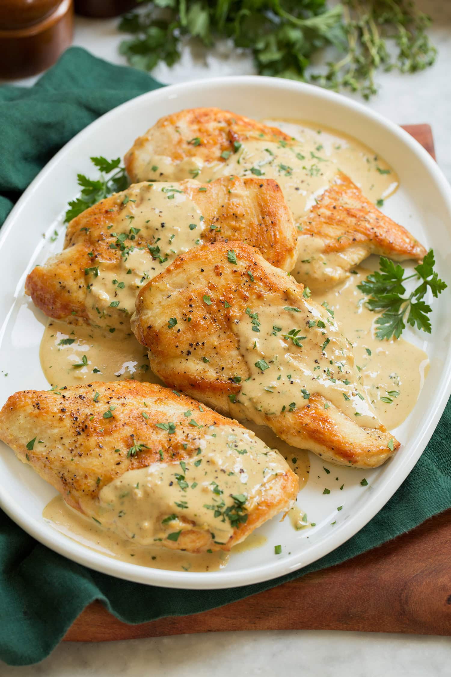 Creamy dijon mustard chicken shown on a white oval serving platter over a green cloth and a wooden tray.