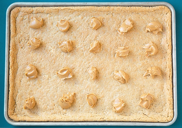 Dollops of peanut butter melting on warm peanut butter bars after baking.