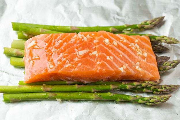 Laying salmon over asparagus on sheet of foil.