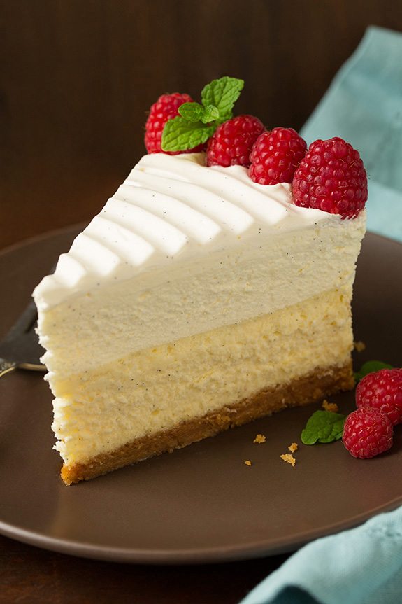 Slice of cheesecake on a brown serving plate, garnished with whipped cream and berries.