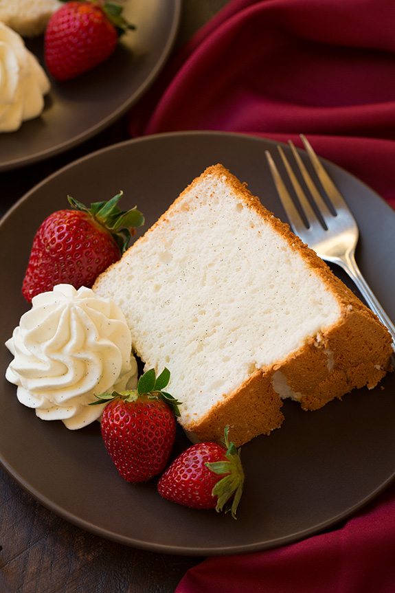 slice of Vanilla Bean Angel Food Cake on plate with whipped cream and strawberries
