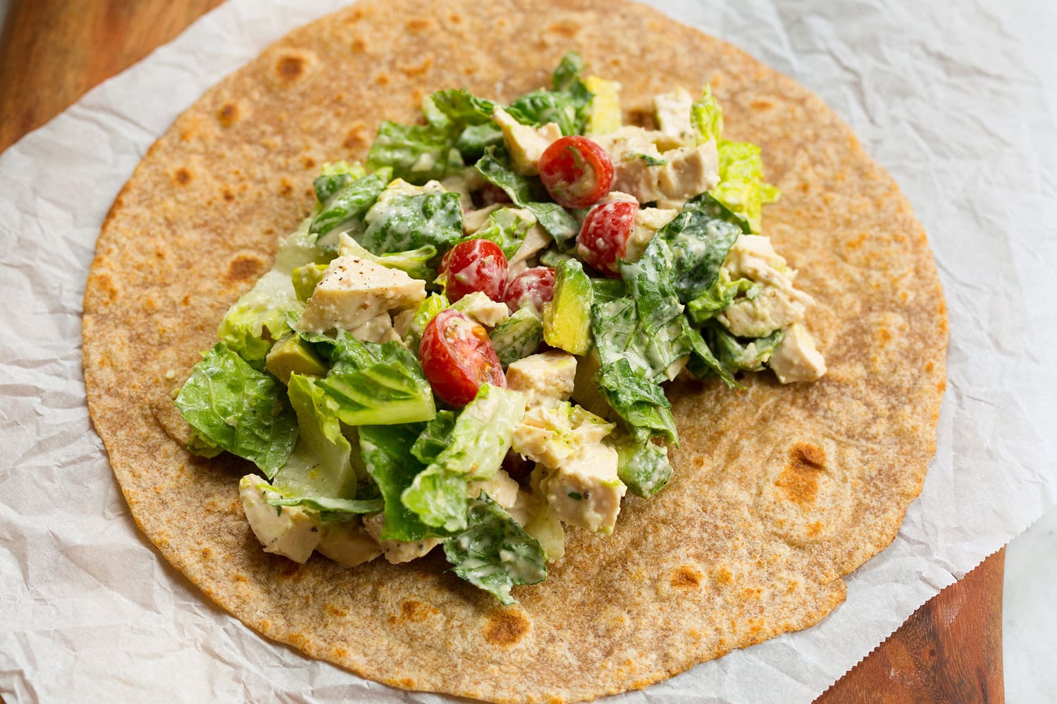 Chicken caesar salad layered over tortilla before wrapping.