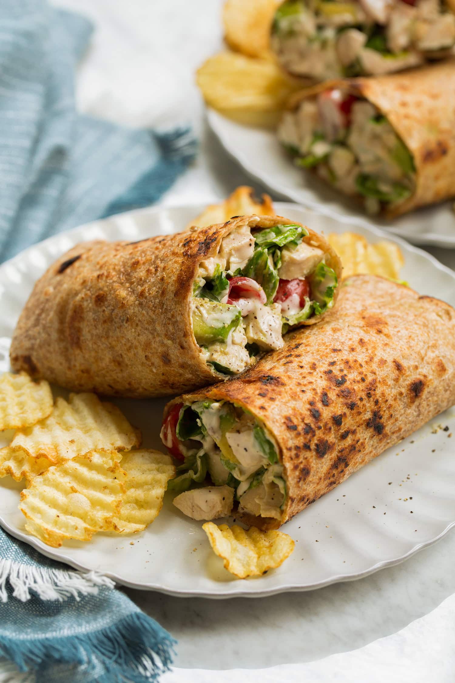 Chicken caesar wrap with avocado and tomato shown served with potato chips.