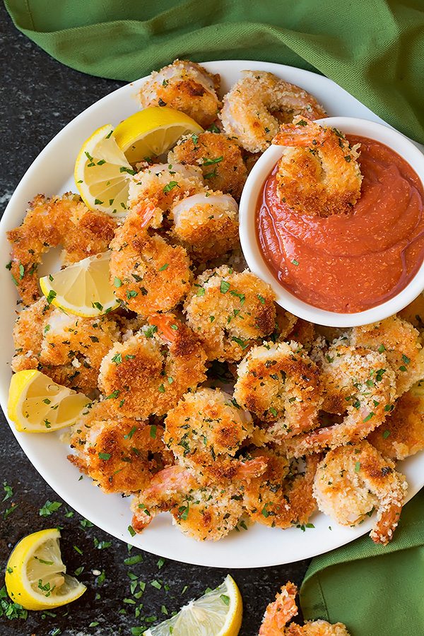 Mound of panko shrimp on a serving plate one shrimp is being dipped in cocktail sauce on the side.