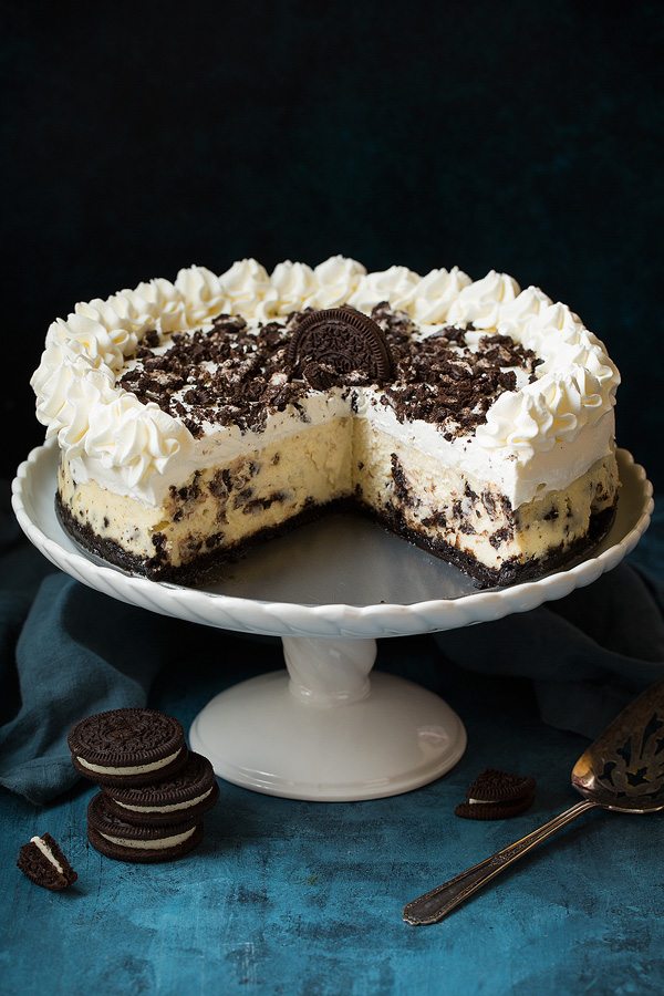Oreo cheesecake on a cake stand with about 1/3 of the cake cut from one section to show inside of cheesecake.