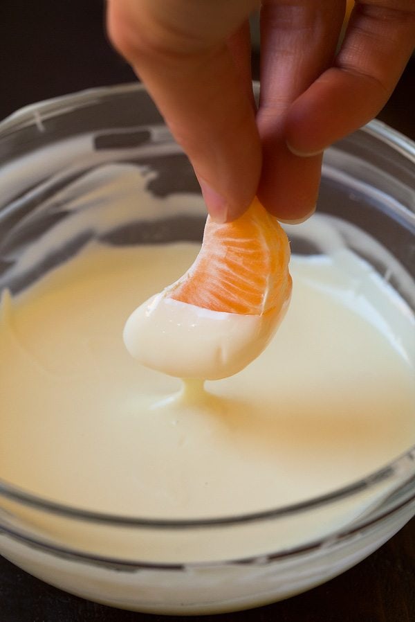 Dipping mandarin orange in melted white chocolate.