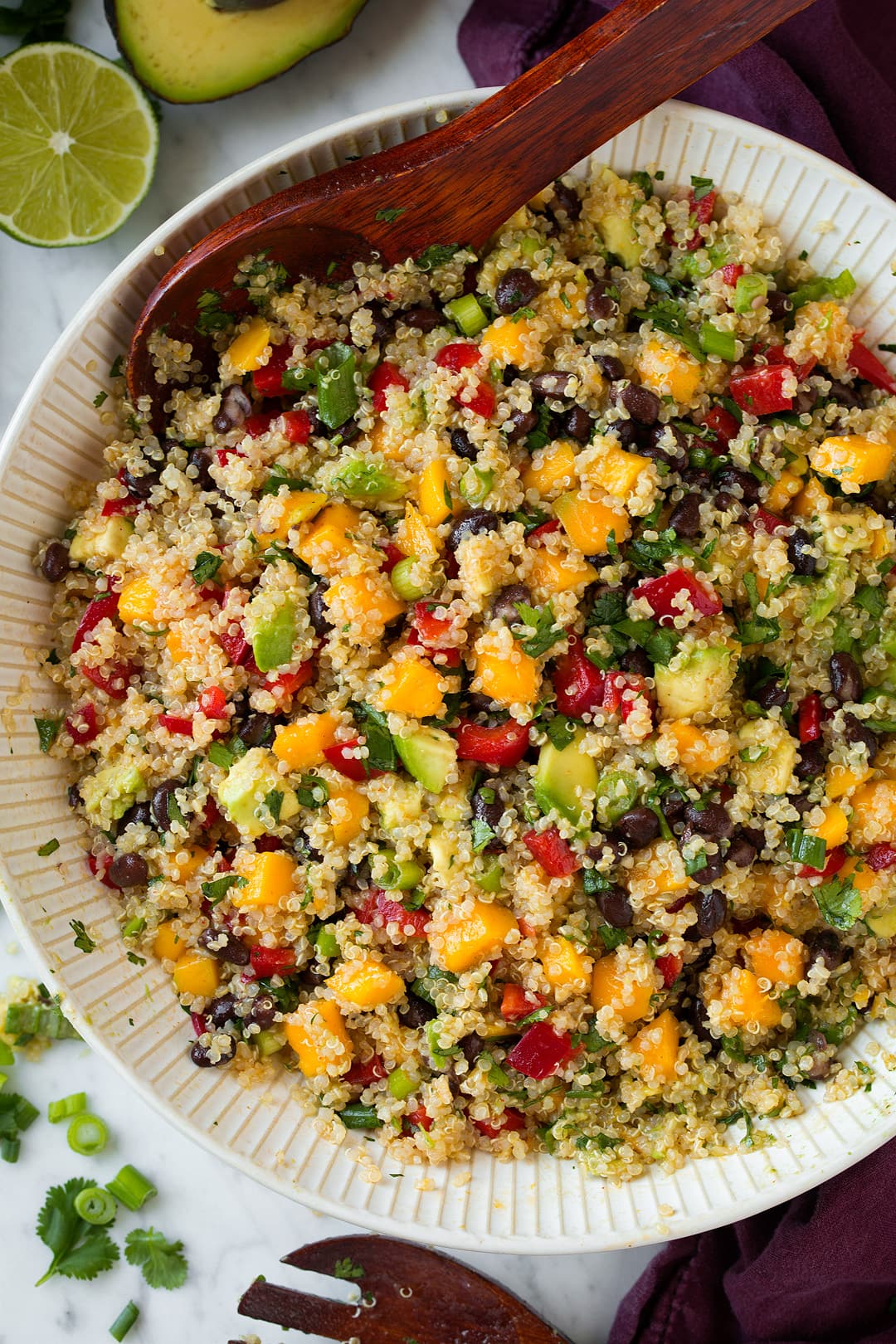 Overhead image of Quinoa Salad in a large white ceramic bowl, with wooden spoon for serving.