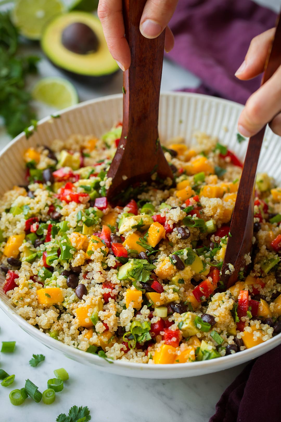Tossing quinoa black bean salad in a large bowl with wooden spoons.