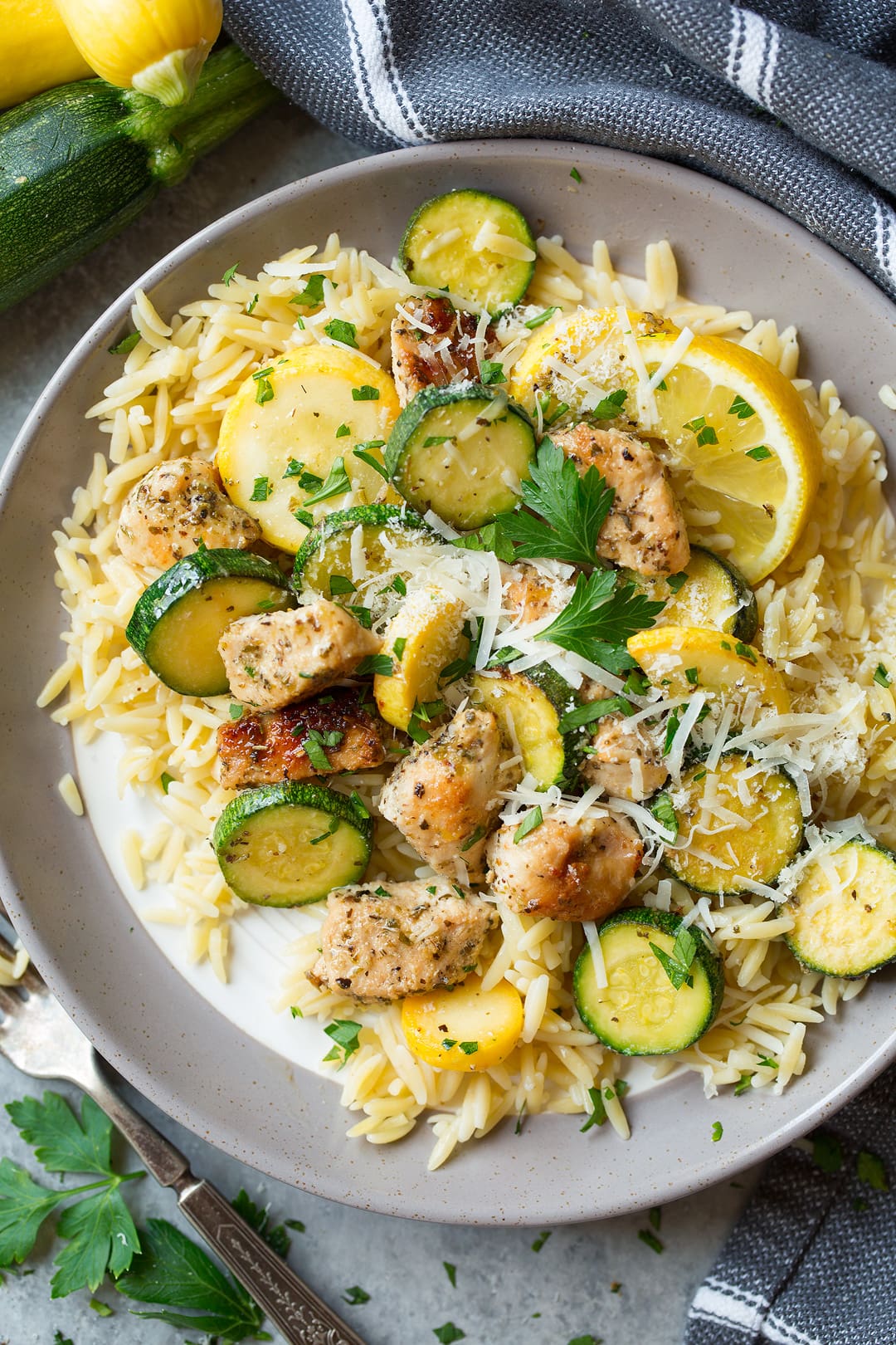 lemon parmesan chicken in skillet with lemon wedges and sliced squash