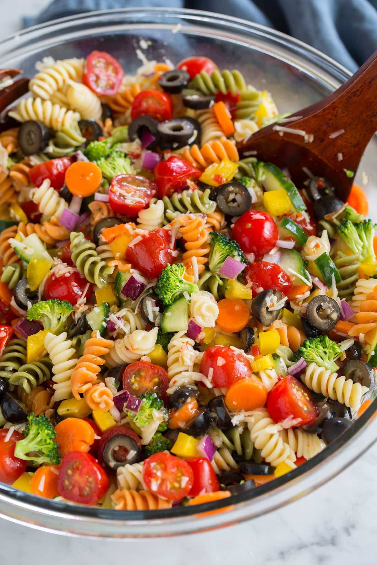 cold pasta salad in a glass bowl with wooden spoon