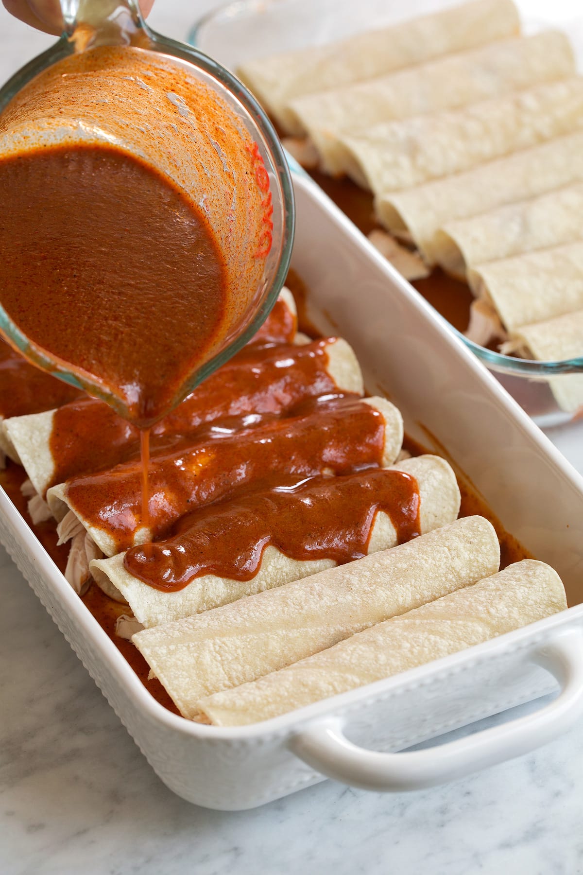 pouring red Enchilada Sauce over a pan of enchiladas 