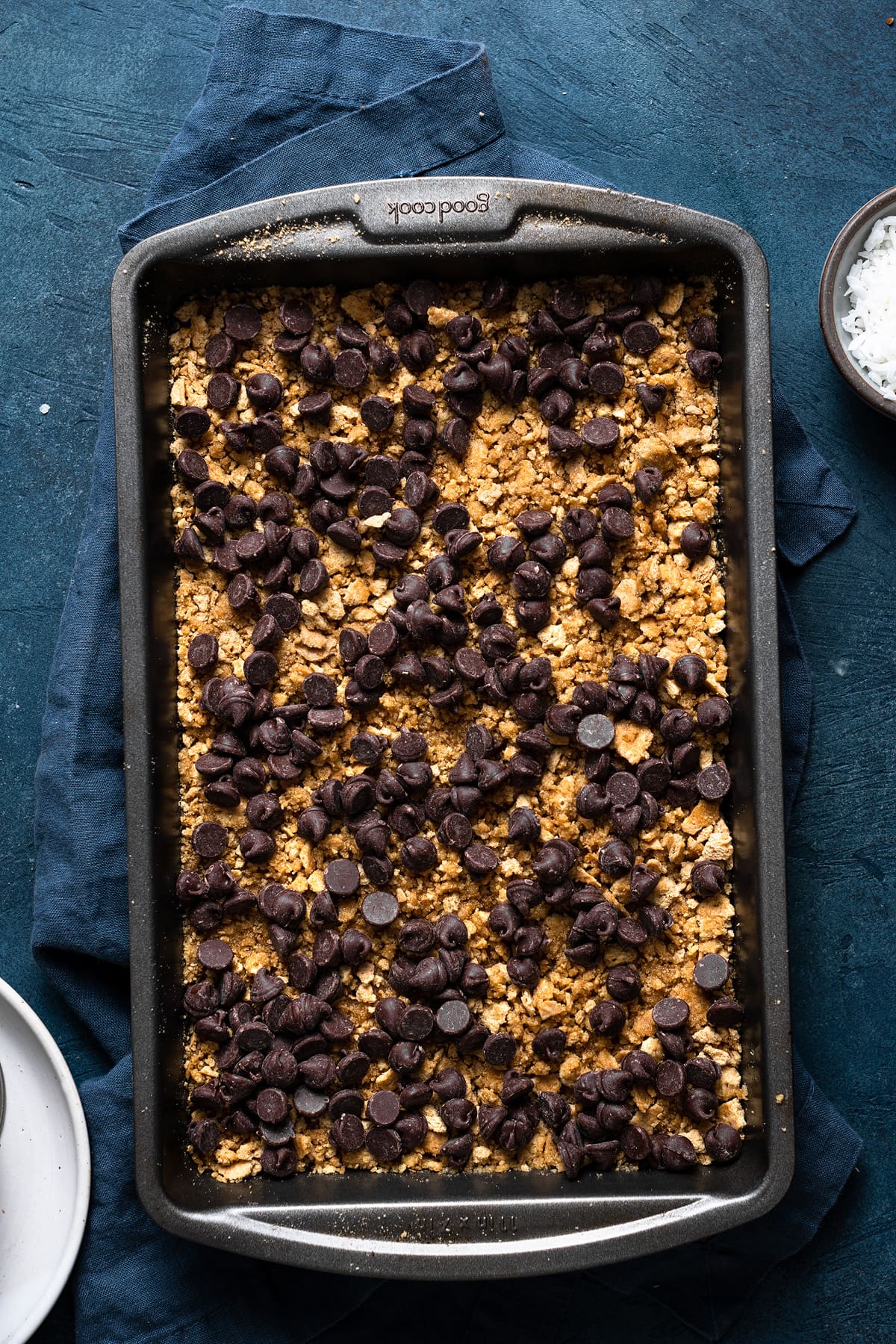 Showing how to make magic 7 layer bars. Sprinkling chocolate chips over graham cracker layer in baking dish.