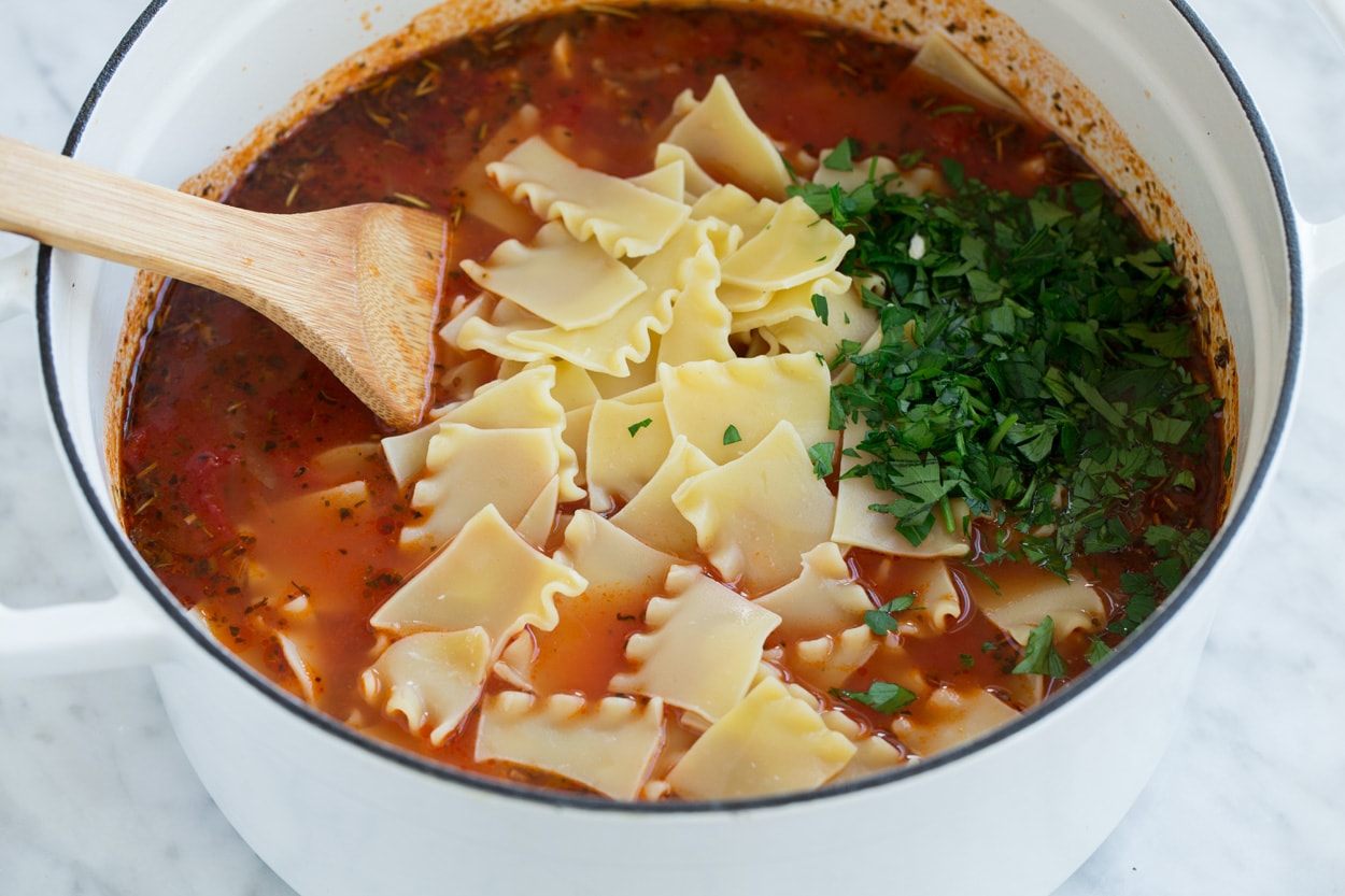 Stirring broken cooked lasagna noodles and parsley into lasagna soup. 