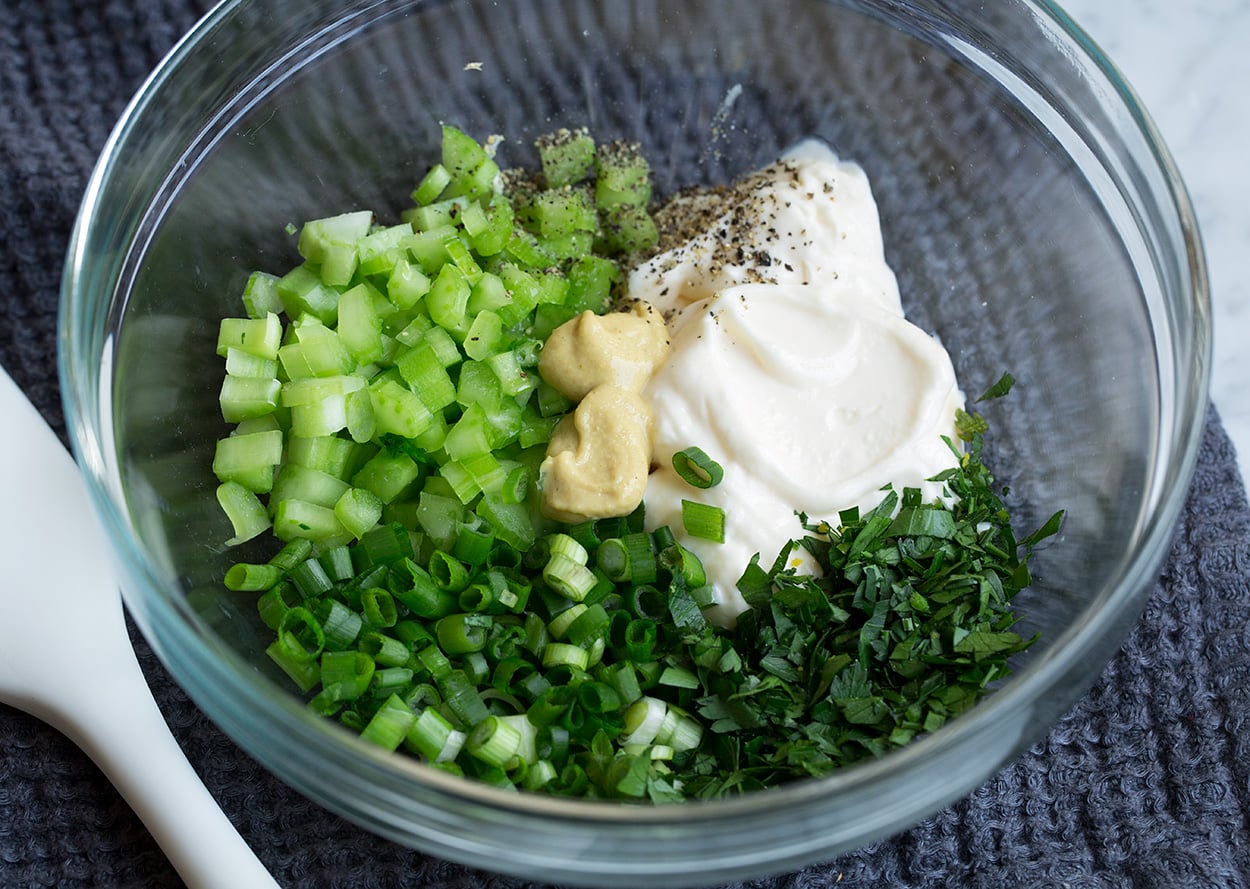 Showing how to make egg salad, mixing mayonnaise, mustard, celery, green onions and parsley in a glass mixing bowl.