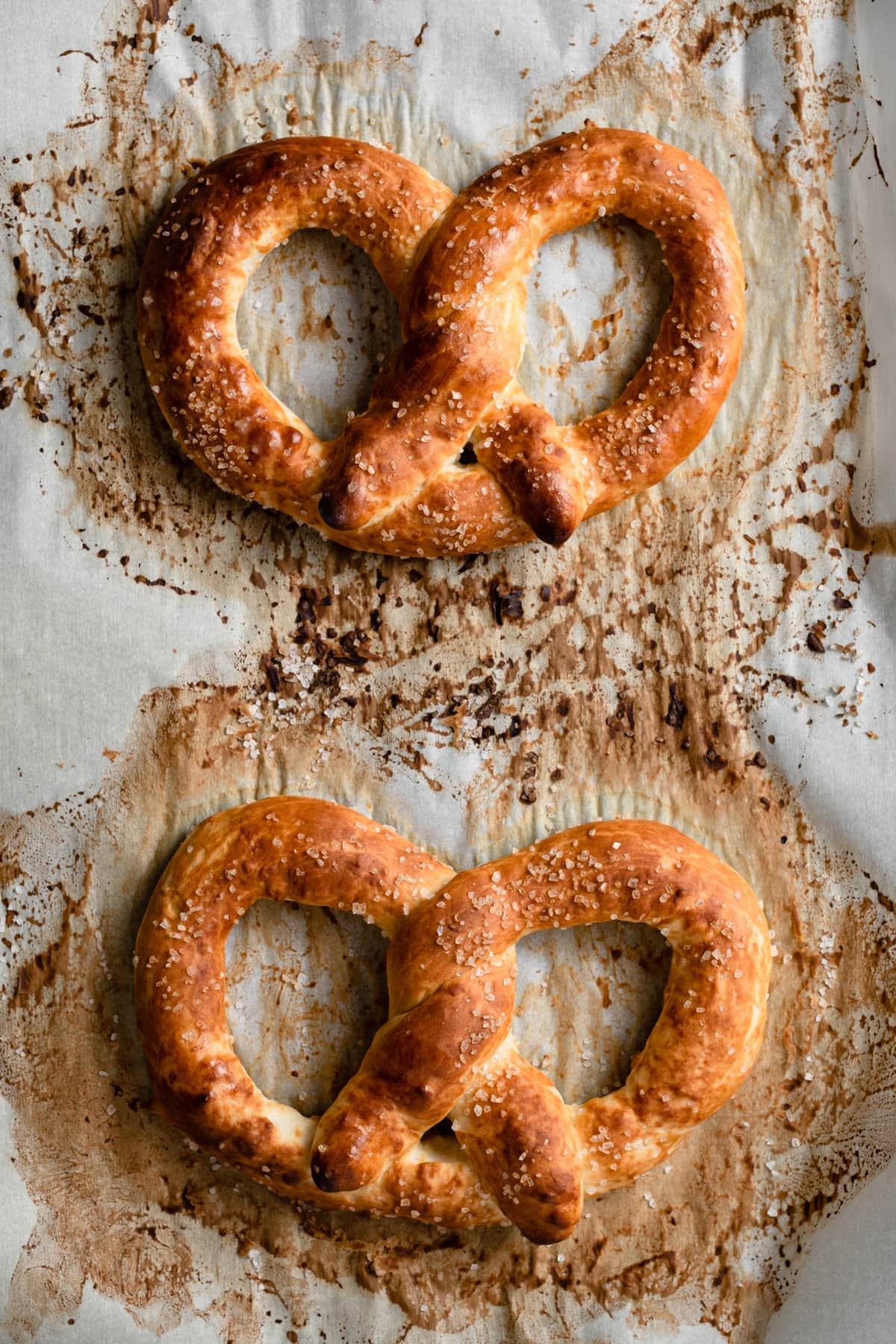 Two pretzels on parchment paper lined baking sheet showing what they should look like after baking with a golden brown color.