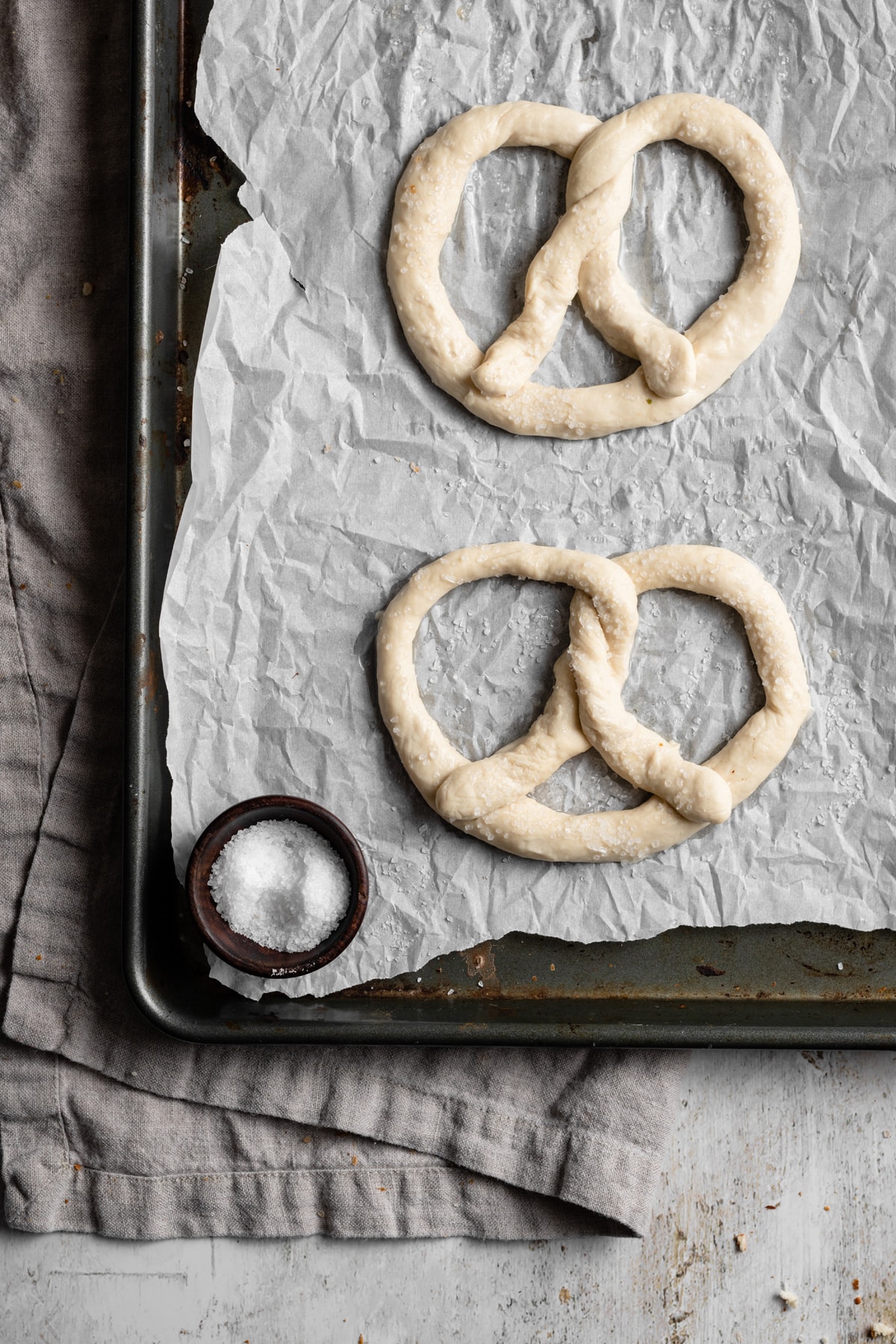 Image showing how to make soft pretzels. Shaping dough into pretzel shapes and they're placed on a parchment paper lined baking sheet to bake.