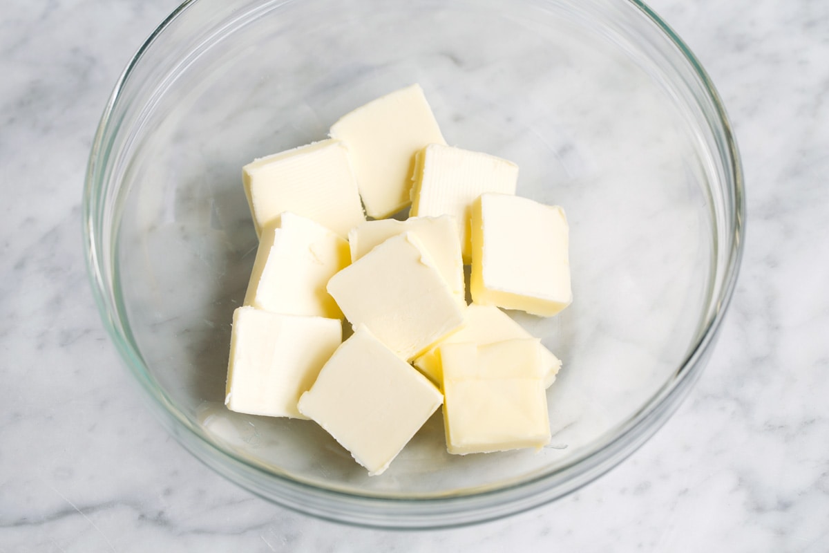 Showing how to make brownies. Adding sliced cubes of butter in glass mixing bowl.