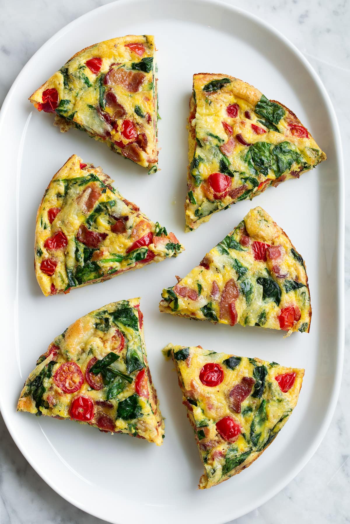 Overhead image of six frittata wedges on a white serving platter.