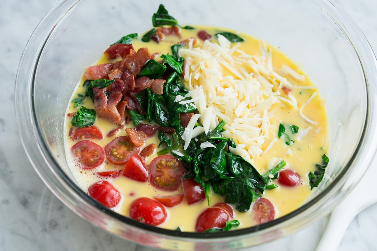 Adding bacon, spinach, tomatoes and swiss to egg mixture for the frittata.