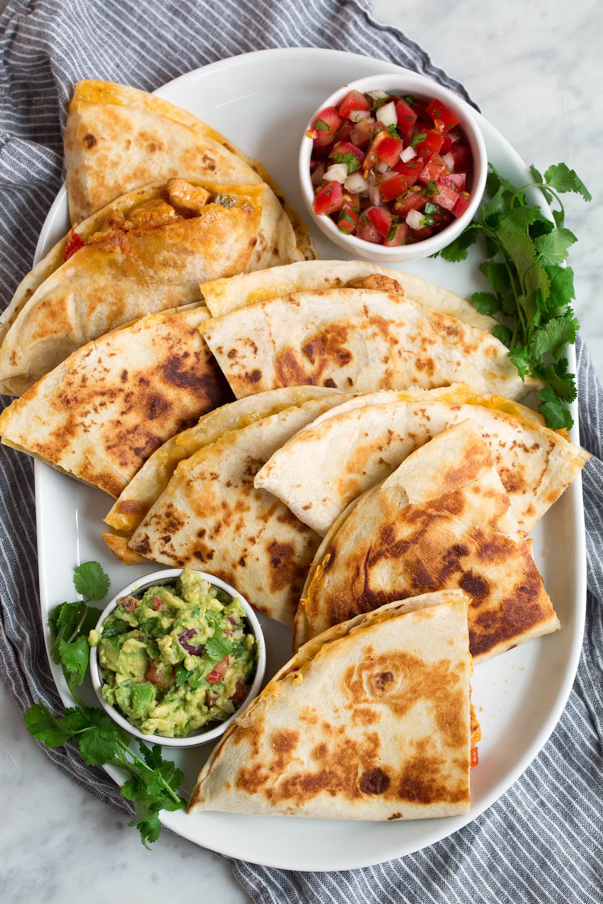 Overhead image of eight quesadilla wedges on a white oblong platter served with pico and guacamole.