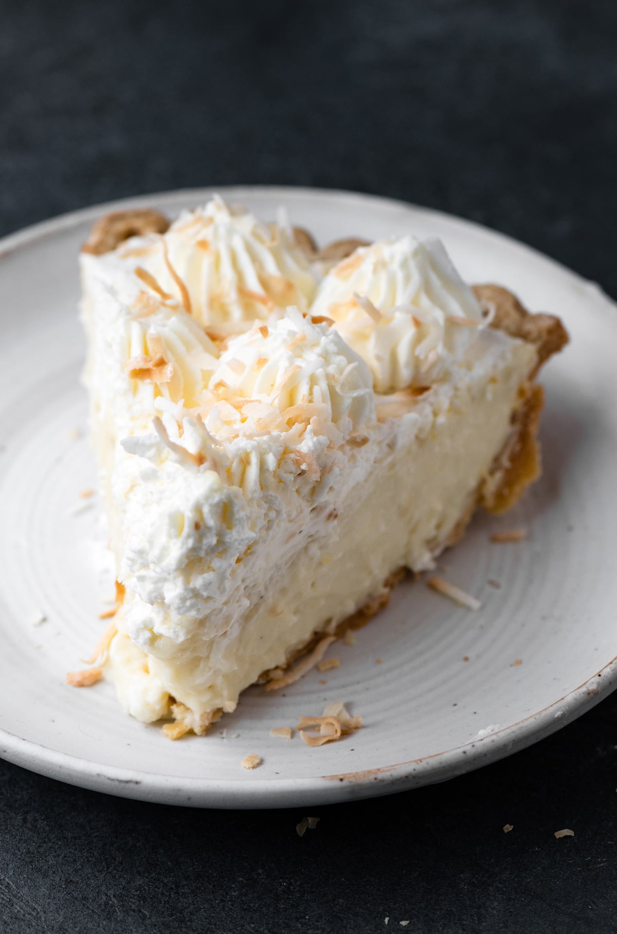 Single slice of coconut cream pie made from scratch on a white dessert plate.