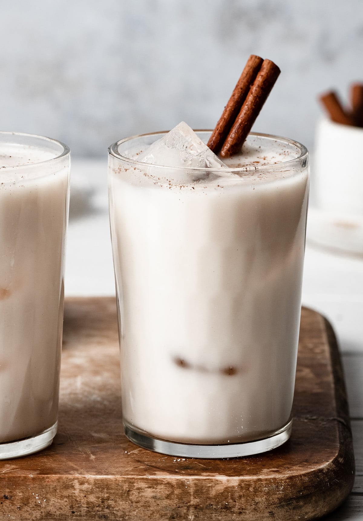 Close up image of horchata in a glass cup with ice cubes and garnished with a cinnamon stick.