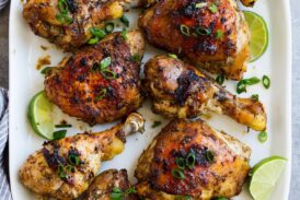 10 pieces of jerk chicken, combination of thighs and legs, on a white oval platter set over a grey surface.
