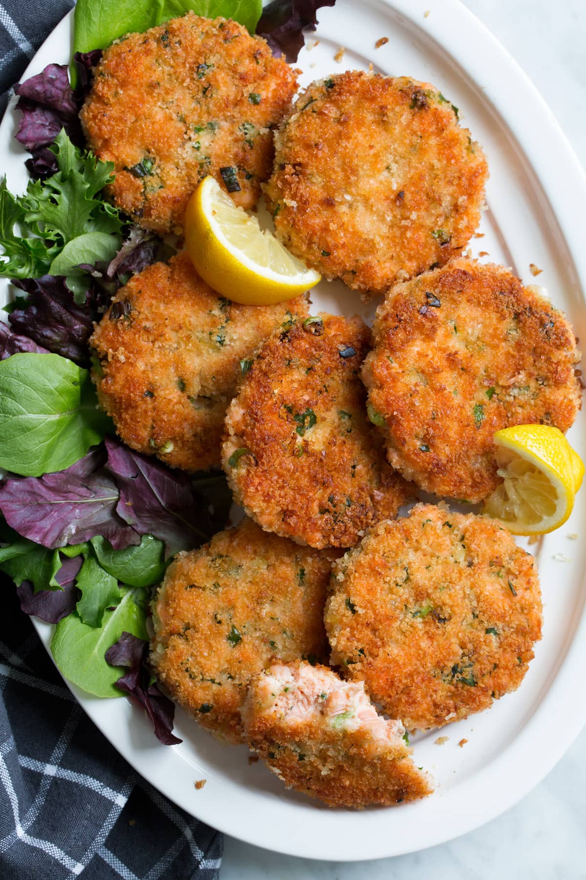 Eight crispy salmon patties on a white serving platter. One is broken in half to show interior.