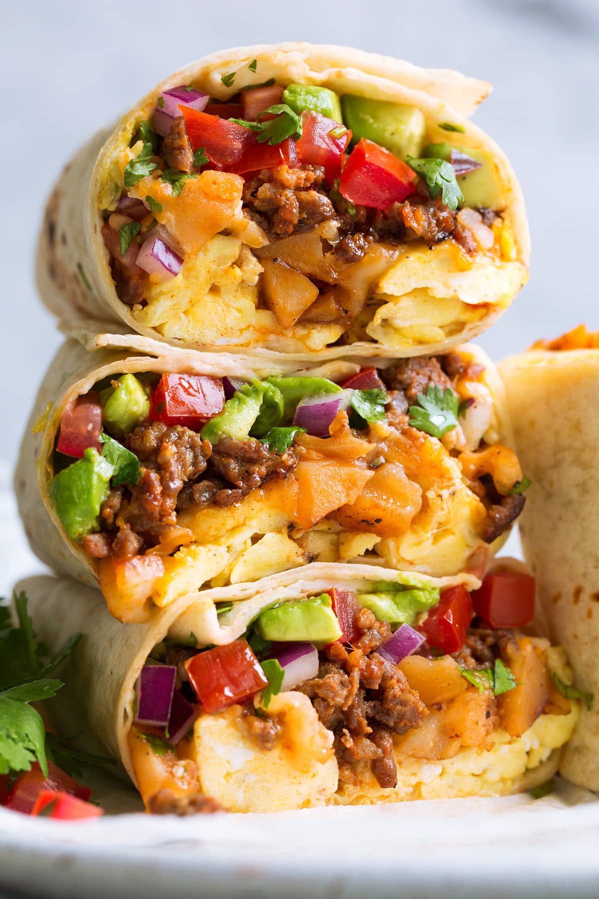 Stack of breakfast burritos with eggs, chorizo sausage, potatoes, cheese, pico de gallo and avocado.