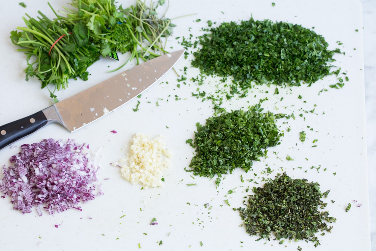 Minching up fresh herbs onion and garlic on a cutting board.