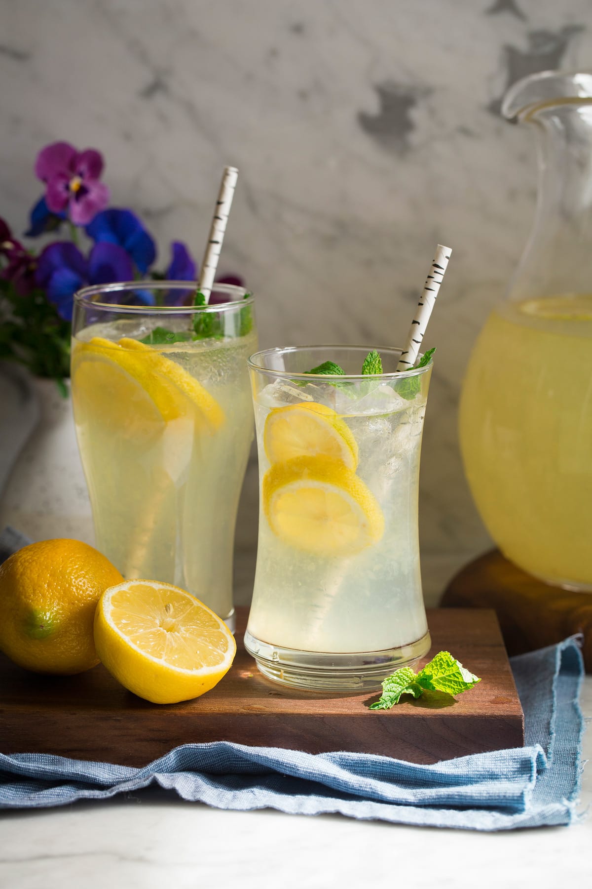 Glass of fresh lemonade in sunshine with flowers in the background.