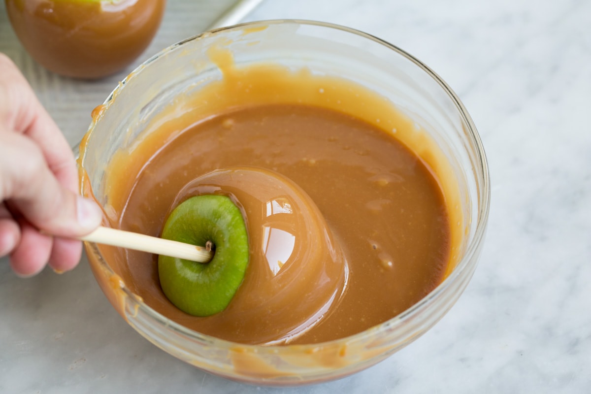 Rolling granny smith apple on stick in melted caramel mixture.