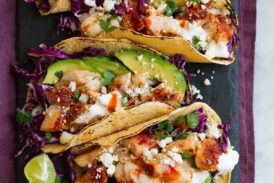 Row of fish tacos on a black slate serving platter.