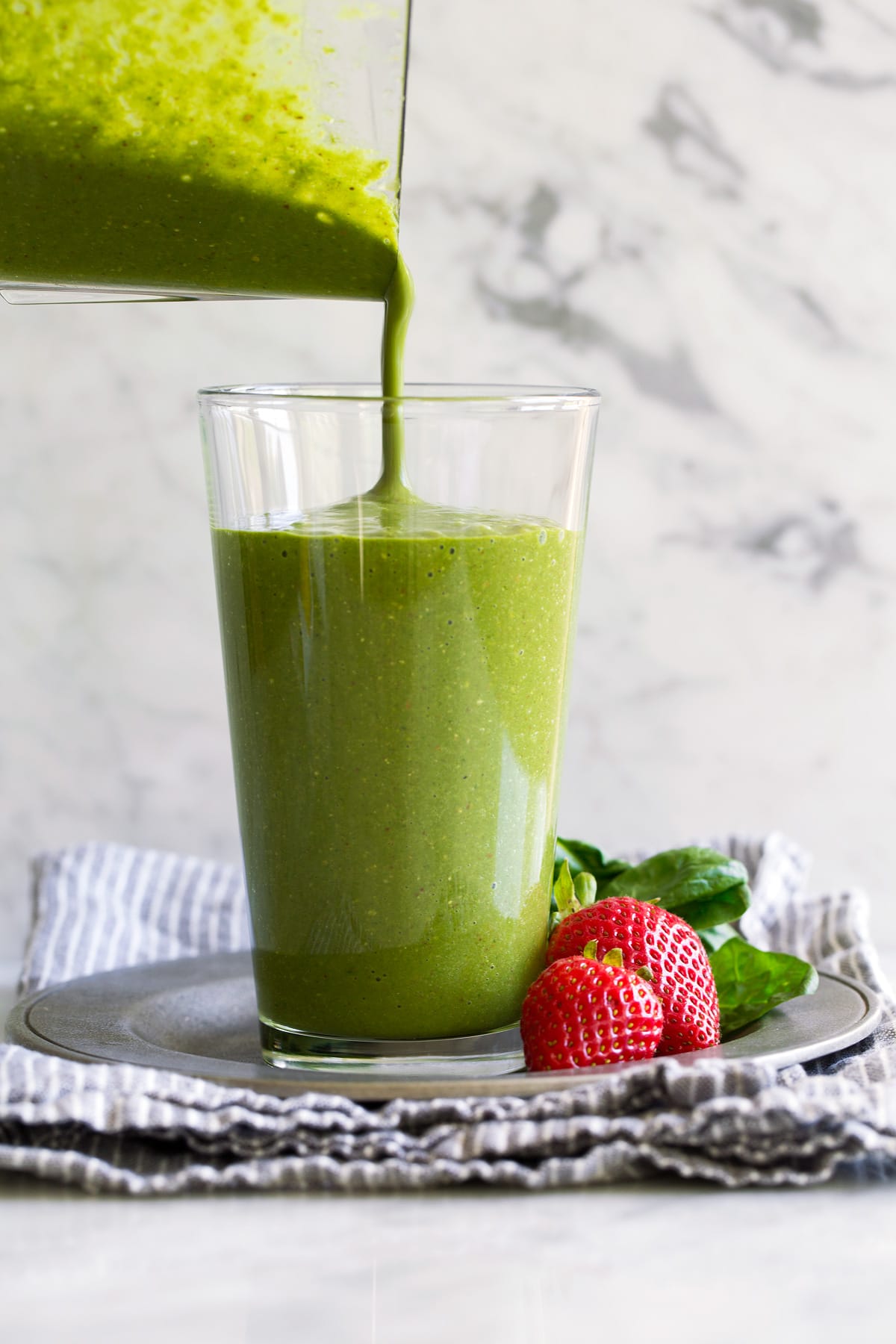 Pouring green smoothie into a glass from a blender jar.