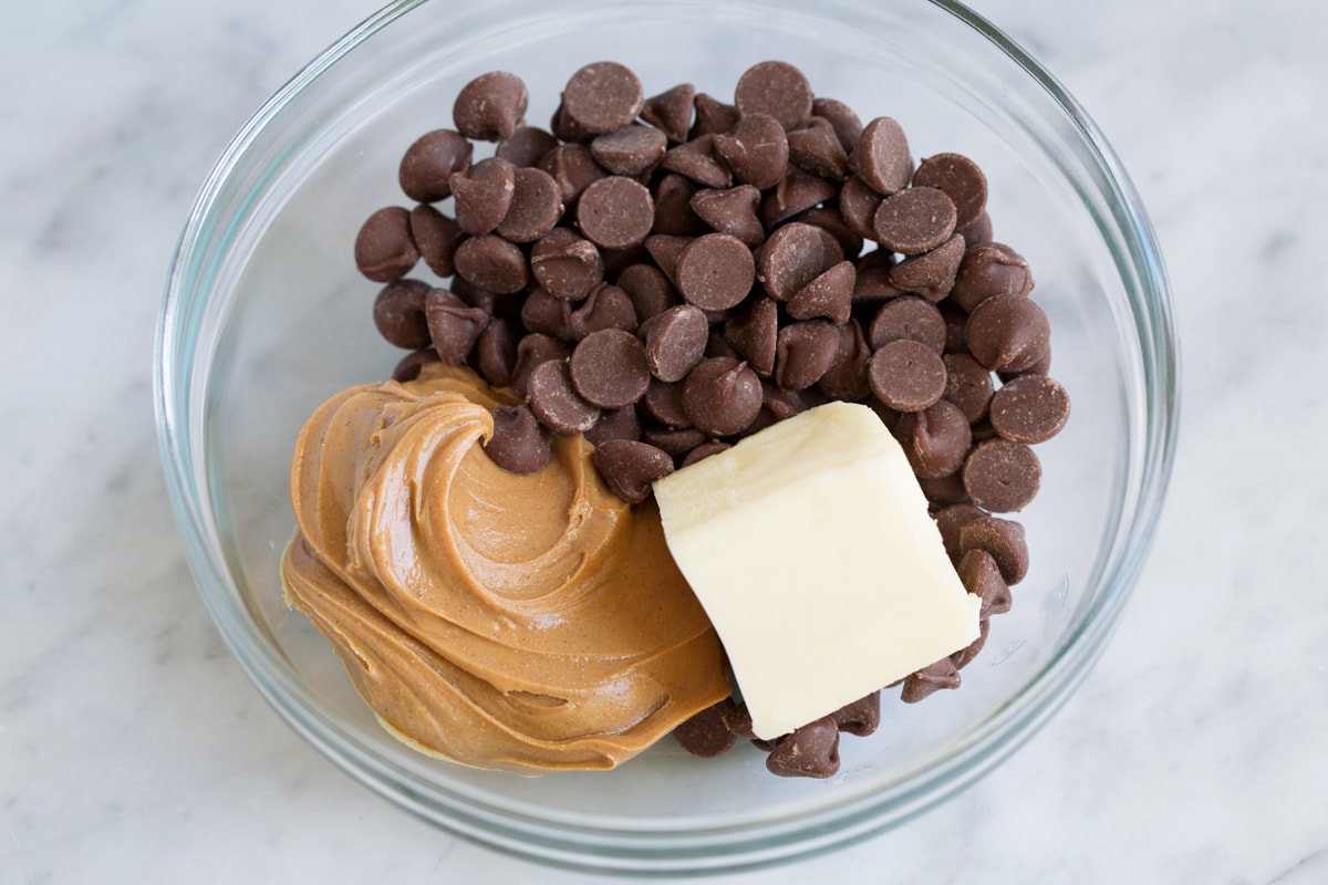 Showing how to make muddy buddies. Adding chocolate chips, peanut butter and butter in a glass mixing bowl.