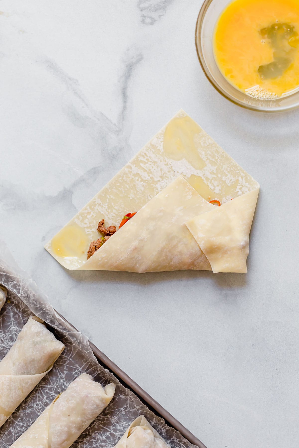 Wrapping egg roll wrapper around filling with egg on edges to seal.