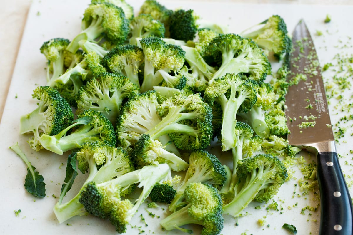 Cutting broccoli florets from stem on a cutting board.