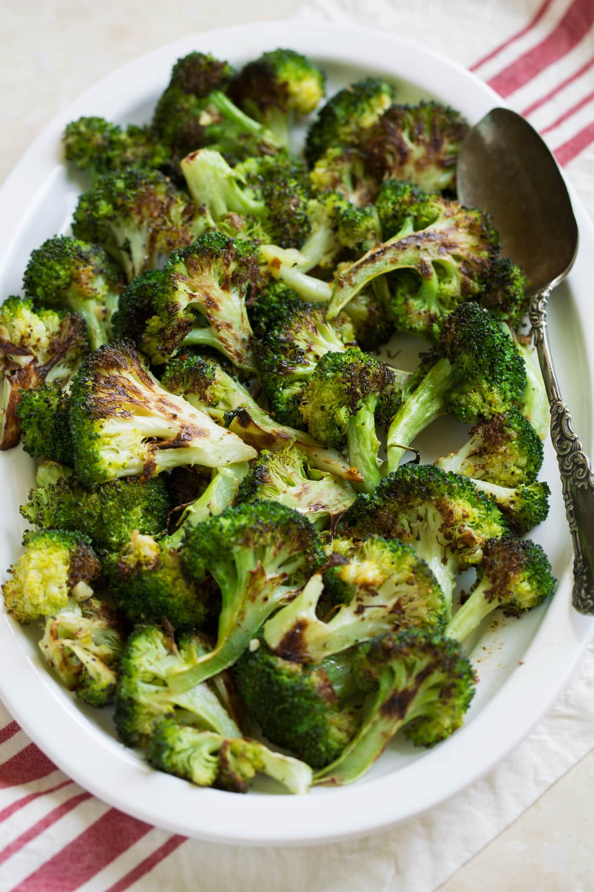 Broccoli on a serving plater over a striped napkin and beige table surface.