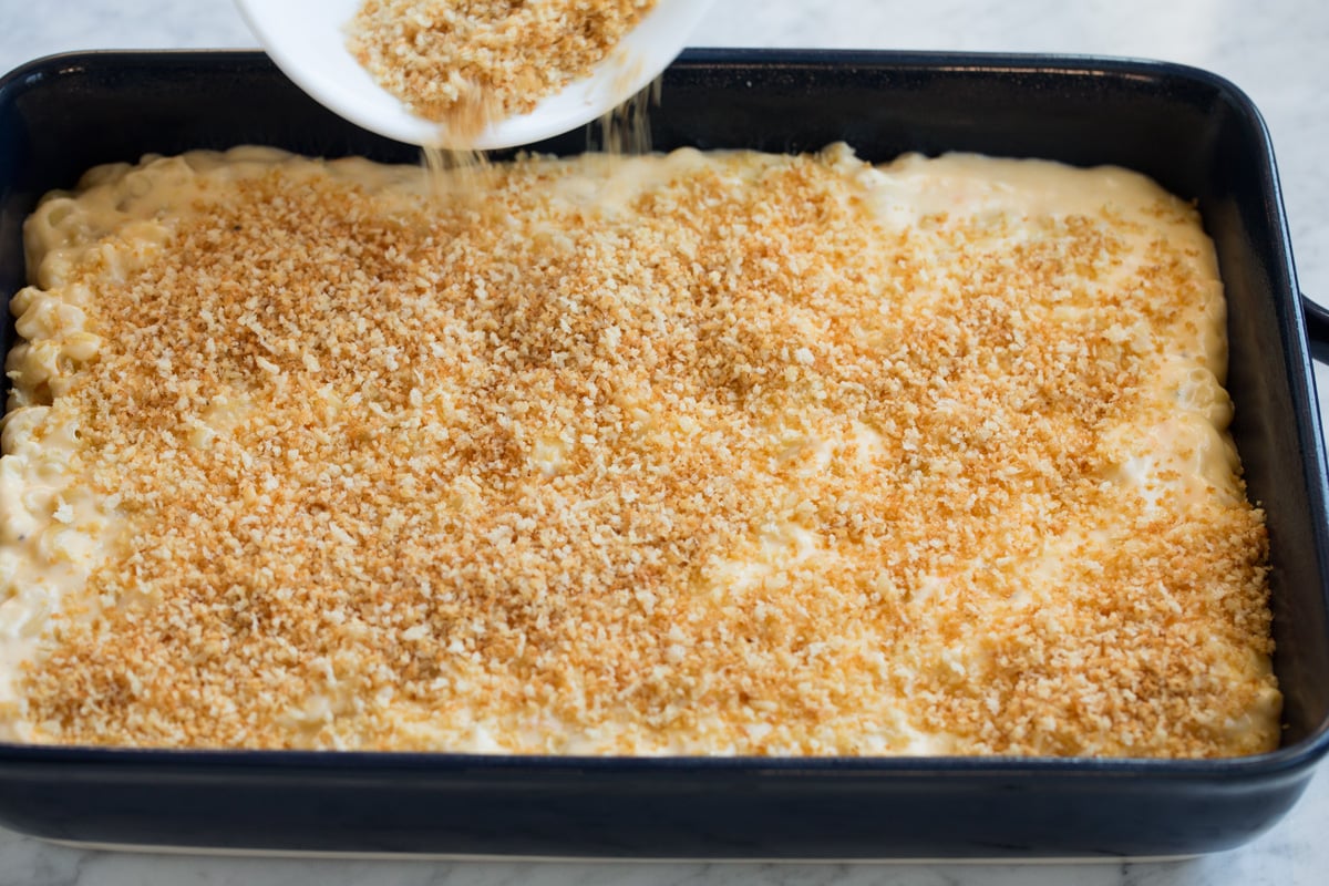Pouring panko topping over macaroni and cheese in baking dish.