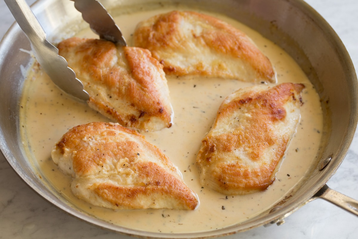Placing chicken breasts into sauce mixture in pan with tongs.