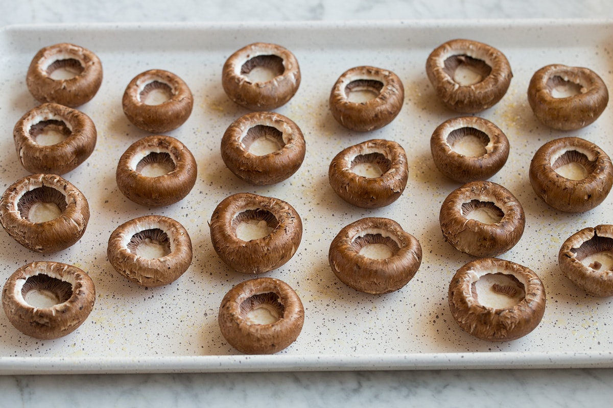 Cremini mushroom caps resting upside down on a baking sheet.