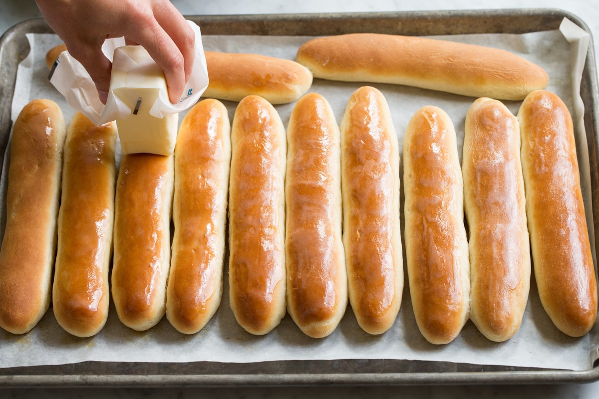 Buttering breadsticks on a baking sheet with a stick of butter. 
