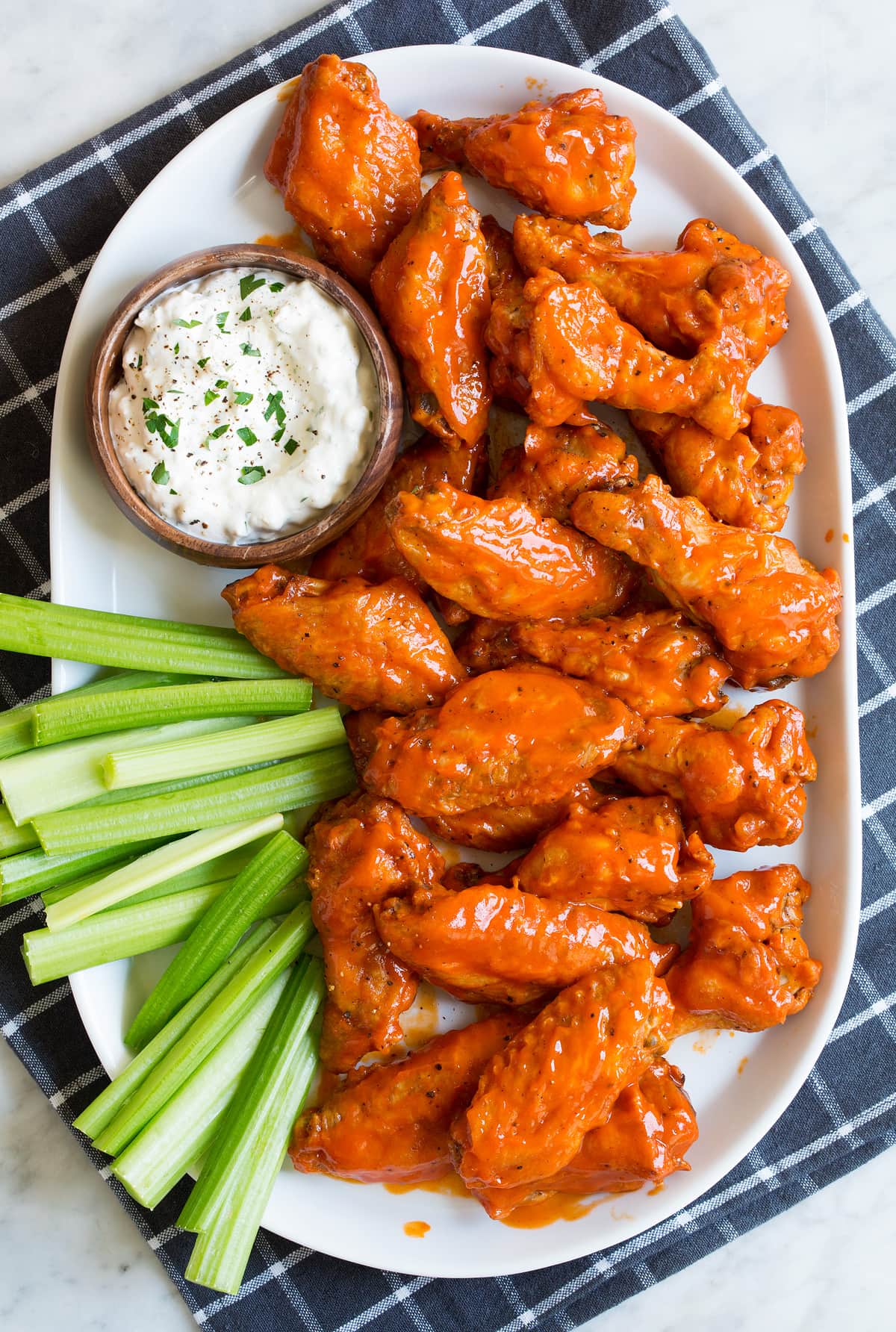 Platter full of buffalo wings coated in a buffalo wing sauce served with a side of blue cheese sauce and celery sticks.